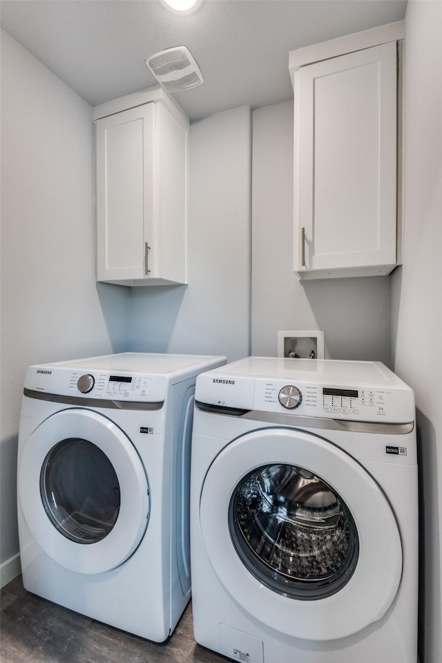 clothes washing area with dark wood-type flooring, washing machine and dryer, and cabinets