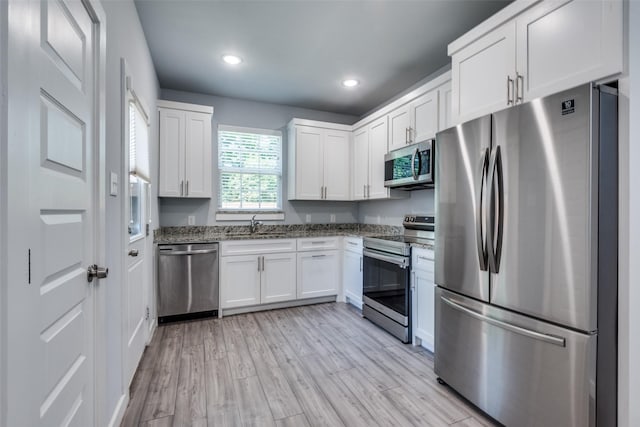 kitchen with sink, light hardwood / wood-style flooring, appliances with stainless steel finishes, white cabinets, and dark stone counters