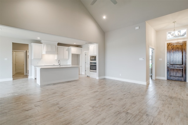 unfurnished living room featuring ceiling fan with notable chandelier, high vaulted ceiling, and light hardwood / wood-style floors