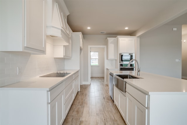 kitchen with white cabinetry, an island with sink, sink, appliances with stainless steel finishes, and light hardwood / wood-style floors