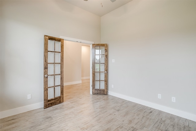 spare room with a towering ceiling, ceiling fan, and light hardwood / wood-style floors