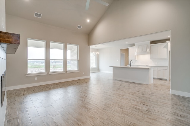 unfurnished living room with ceiling fan with notable chandelier, high vaulted ceiling, light hardwood / wood-style floors, and sink