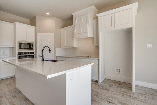 kitchen with stainless steel appliances, a center island with sink, sink, white cabinetry, and light hardwood / wood-style flooring