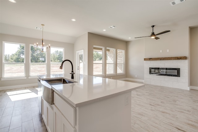 kitchen with an island with sink, white cabinets, decorative light fixtures, and light wood-type flooring