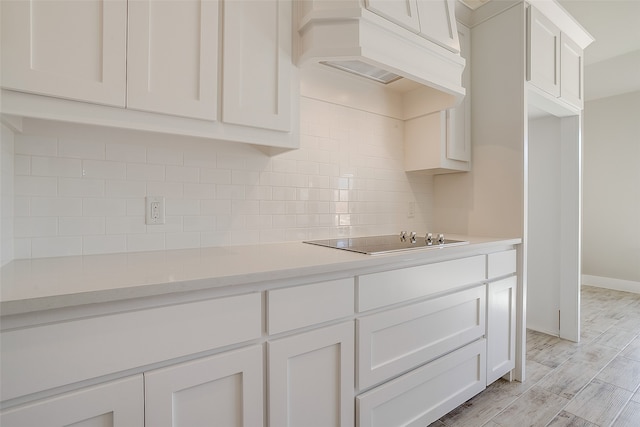 kitchen featuring ventilation hood, decorative backsplash, light hardwood / wood-style floors, white cabinets, and black electric cooktop