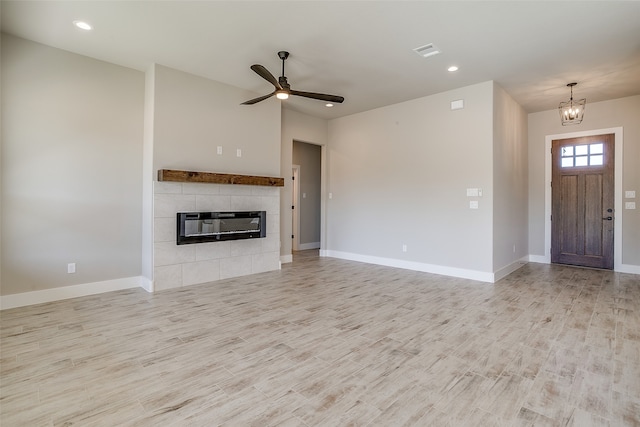 unfurnished living room featuring ceiling fan with notable chandelier, a tile fireplace, and light hardwood / wood-style flooring