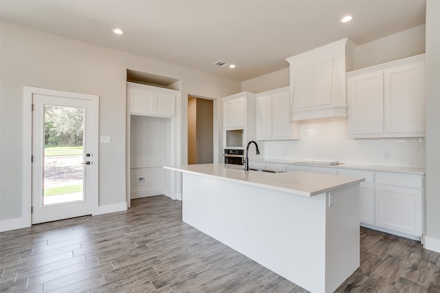 kitchen featuring white cabinets, sink, a kitchen island with sink, light wood-type flooring, and decorative backsplash