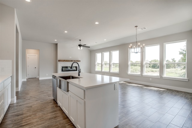 kitchen featuring hanging light fixtures, white cabinetry, an island with sink, ceiling fan with notable chandelier, and sink