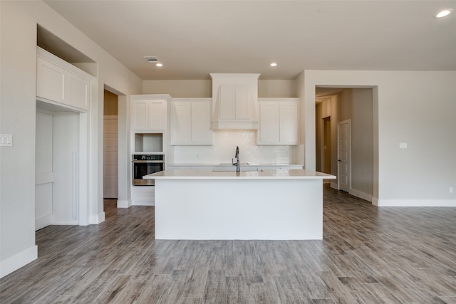 kitchen with an island with sink, light wood-type flooring, white cabinetry, and stainless steel oven