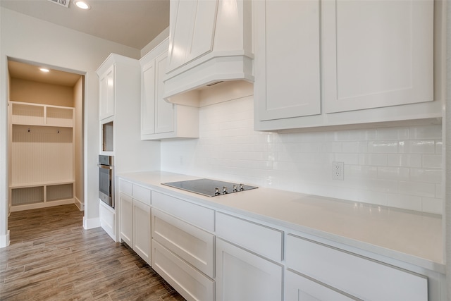 kitchen with black electric cooktop, white cabinets, oven, dark hardwood / wood-style flooring, and premium range hood