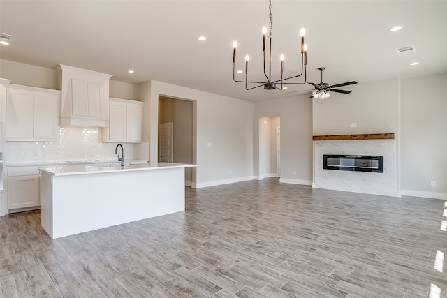 kitchen featuring light wood-type flooring, ceiling fan with notable chandelier, white cabinetry, and a premium fireplace