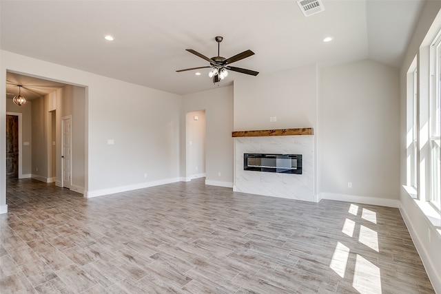 unfurnished living room featuring light wood-type flooring, ceiling fan with notable chandelier, a premium fireplace, and lofted ceiling