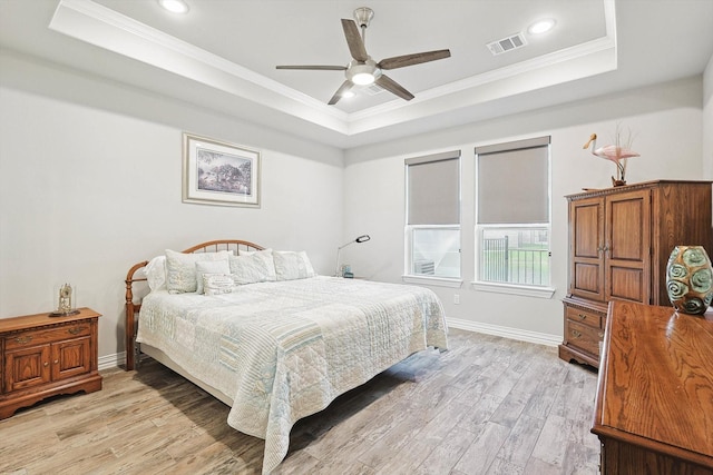 bedroom with ornamental molding, light hardwood / wood-style floors, and a tray ceiling