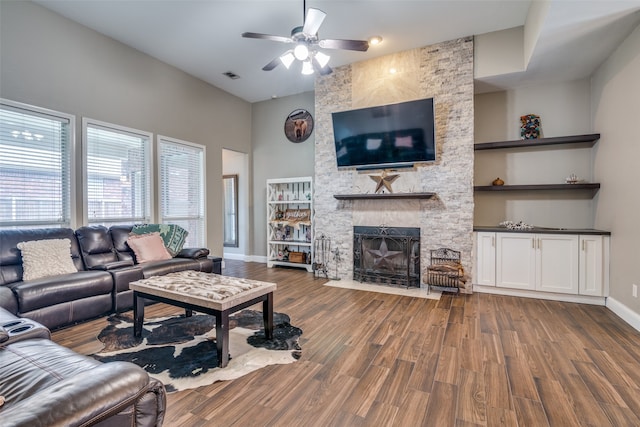 living room with hardwood / wood-style flooring, built in features, a stone fireplace, and ceiling fan