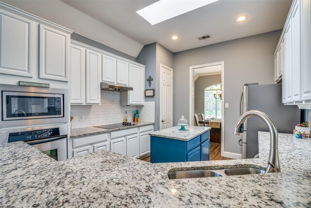 kitchen featuring a skylight, a kitchen island, appliances with stainless steel finishes, hardwood / wood-style flooring, and sink