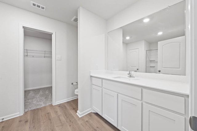 bathroom with walk in shower, hardwood / wood-style floors, vanity, and toilet