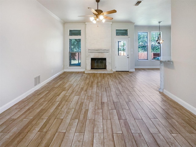 unfurnished living room with light wood-type flooring, ceiling fan with notable chandelier, ornamental molding, and a large fireplace