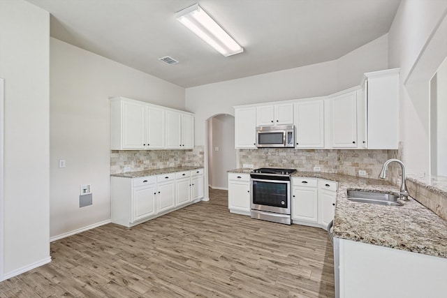 kitchen with appliances with stainless steel finishes, tasteful backsplash, light stone counters, sink, and white cabinets