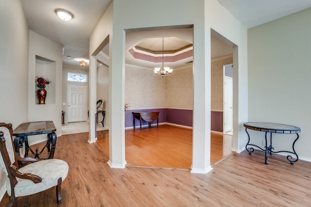 entrance foyer with crown molding, a notable chandelier, light hardwood / wood-style flooring, and a tray ceiling