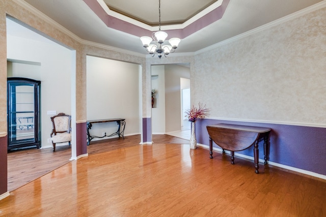 living area featuring ornamental molding, a raised ceiling, hardwood / wood-style floors, and a chandelier