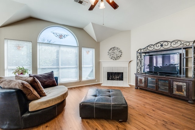 living room featuring a tile fireplace, hardwood / wood-style flooring, vaulted ceiling, and ceiling fan