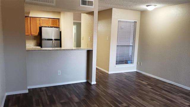 kitchen featuring stainless steel fridge, light stone countertops, dark hardwood / wood-style flooring, and a textured ceiling