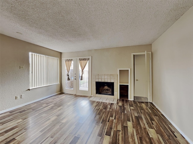 unfurnished living room with wood-type flooring, a tile fireplace, french doors, and a textured ceiling