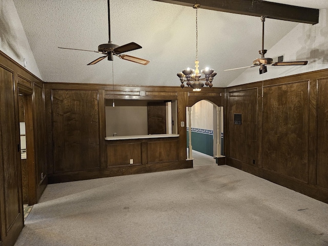 unfurnished living room with ceiling fan with notable chandelier, a textured ceiling, light colored carpet, wooden walls, and vaulted ceiling with beams