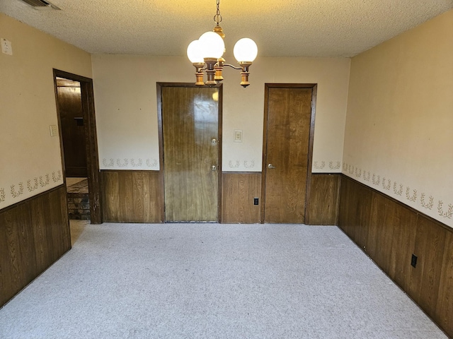 unfurnished room with wood walls, carpet, a textured ceiling, and a notable chandelier