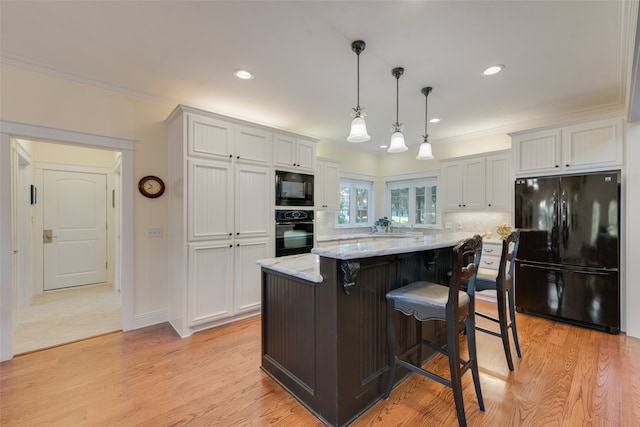 kitchen featuring white cabinets, light hardwood / wood-style flooring, a center island, and black appliances