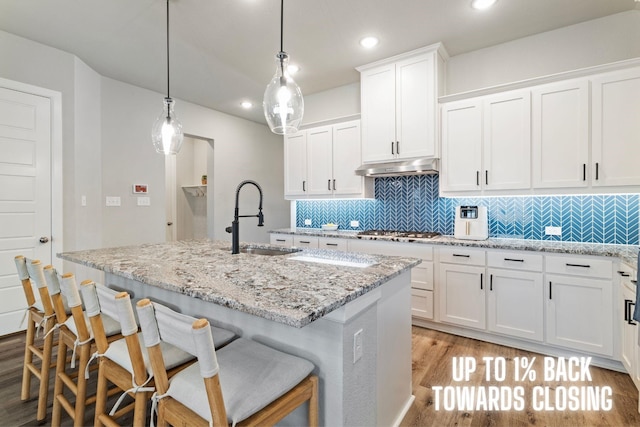 kitchen featuring a center island with sink, sink, hanging light fixtures, stainless steel gas cooktop, and white cabinets