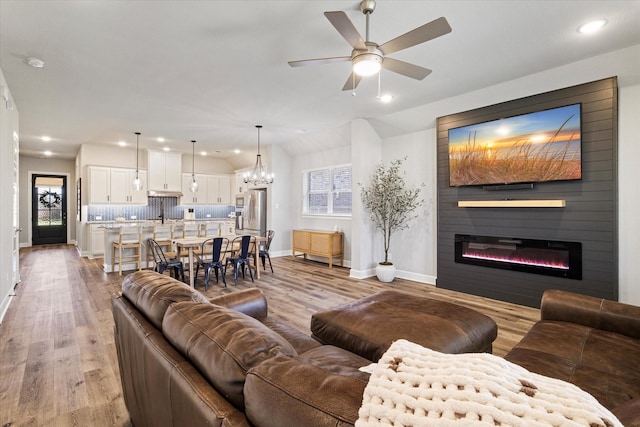 living room with light wood-type flooring, ceiling fan with notable chandelier, a fireplace, and sink