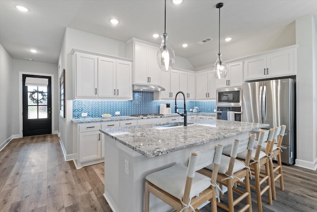 kitchen featuring appliances with stainless steel finishes, decorative light fixtures, white cabinetry, sink, and a kitchen island with sink