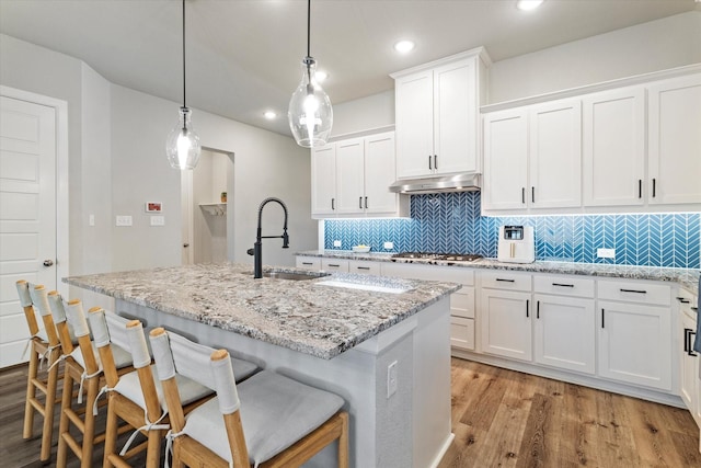 kitchen with pendant lighting, white cabinetry, sink, a kitchen island with sink, and a breakfast bar area