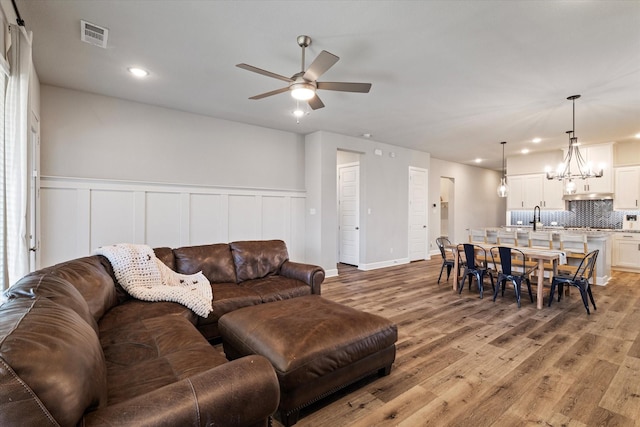 living room featuring ceiling fan with notable chandelier and light hardwood / wood-style flooring