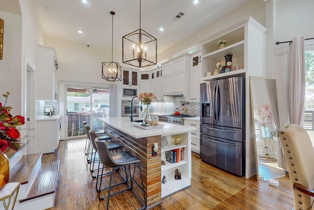 kitchen featuring backsplash, appliances with stainless steel finishes, decorative light fixtures, a kitchen island, and white cabinetry