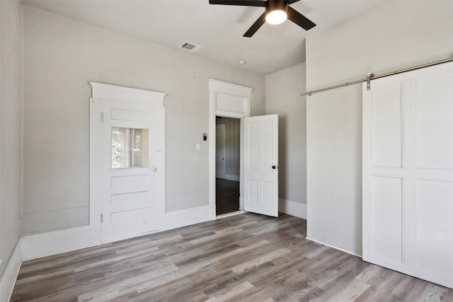 unfurnished bedroom with light hardwood / wood-style floors, a barn door, and ceiling fan