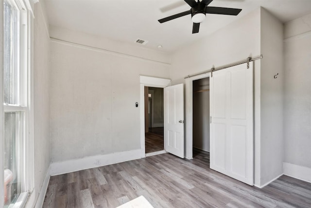 unfurnished bedroom featuring a closet, a barn door, ceiling fan, and light wood-type flooring