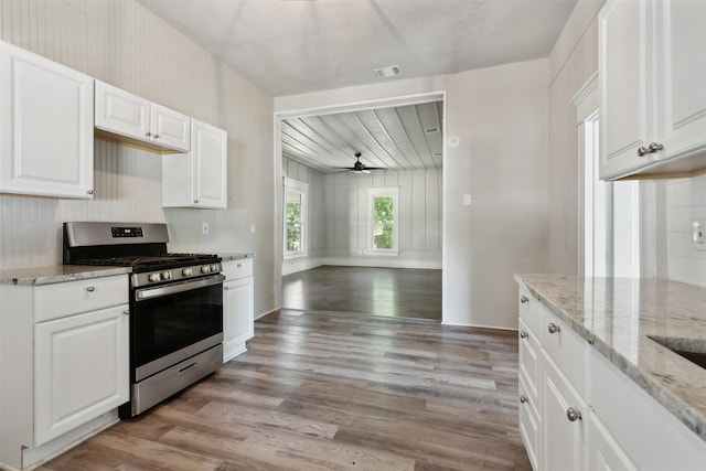 kitchen featuring stainless steel gas stove, light stone counters, white cabinets, and light wood-type flooring