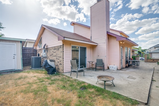 back of property with cooling unit, a fire pit, a storage unit, a patio area, and a yard