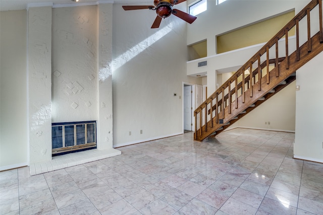 unfurnished living room featuring a brick fireplace, a high ceiling, and ceiling fan