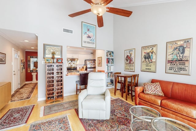 living room with ceiling fan, light hardwood / wood-style floors, crown molding, and a towering ceiling