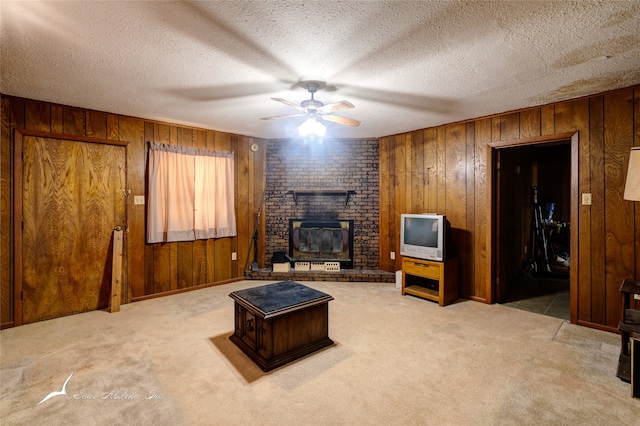 living room with carpet flooring, a textured ceiling, wood walls, ceiling fan, and a fireplace