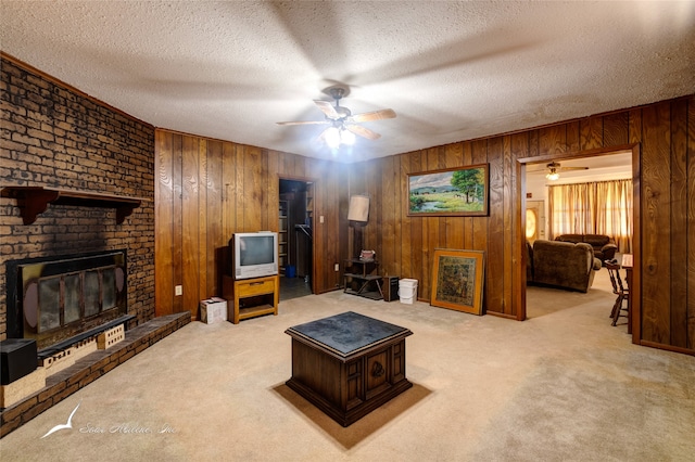 carpeted living room featuring ceiling fan, wooden walls, a textured ceiling, and a brick fireplace