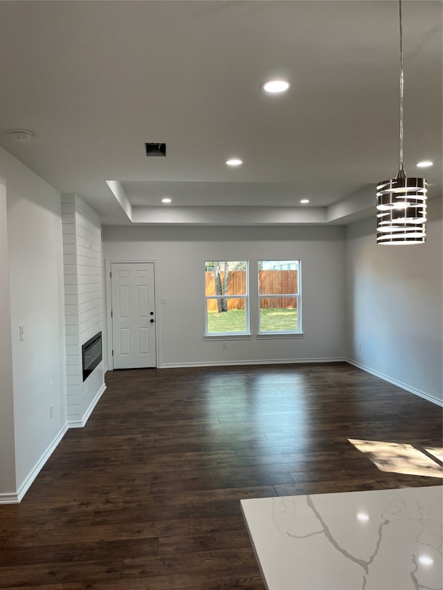 unfurnished living room with an inviting chandelier, dark wood-type flooring, a tray ceiling, and a large fireplace