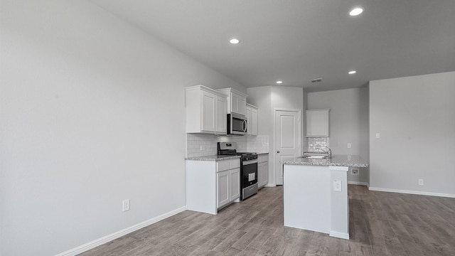 kitchen with a center island with sink, stainless steel appliances, light stone counters, light wood-type flooring, and white cabinets