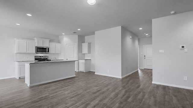 kitchen with light stone countertops, a center island with sink, wood-type flooring, appliances with stainless steel finishes, and white cabinetry