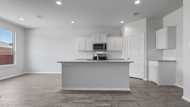 kitchen with appliances with stainless steel finishes, light hardwood / wood-style floors, an island with sink, white cabinetry, and light stone counters