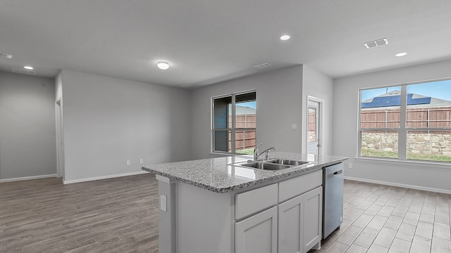 kitchen featuring light stone countertops, light hardwood / wood-style flooring, dishwasher, a kitchen island with sink, and sink