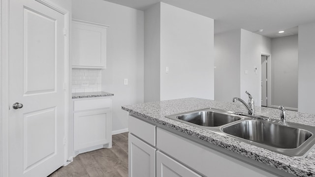 kitchen with light stone countertops, light hardwood / wood-style floors, tasteful backsplash, sink, and white cabinets